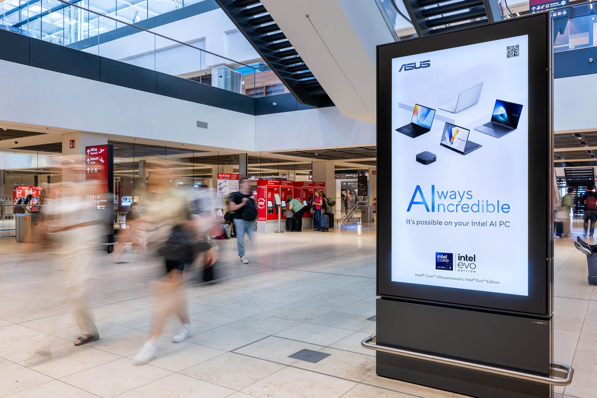 Am Flughafen BER steht ein digitales City Light Poster, welches zur IFA Messe die Werbung von ASUS zeigt. Links im Hintergrund laufen Menschen.