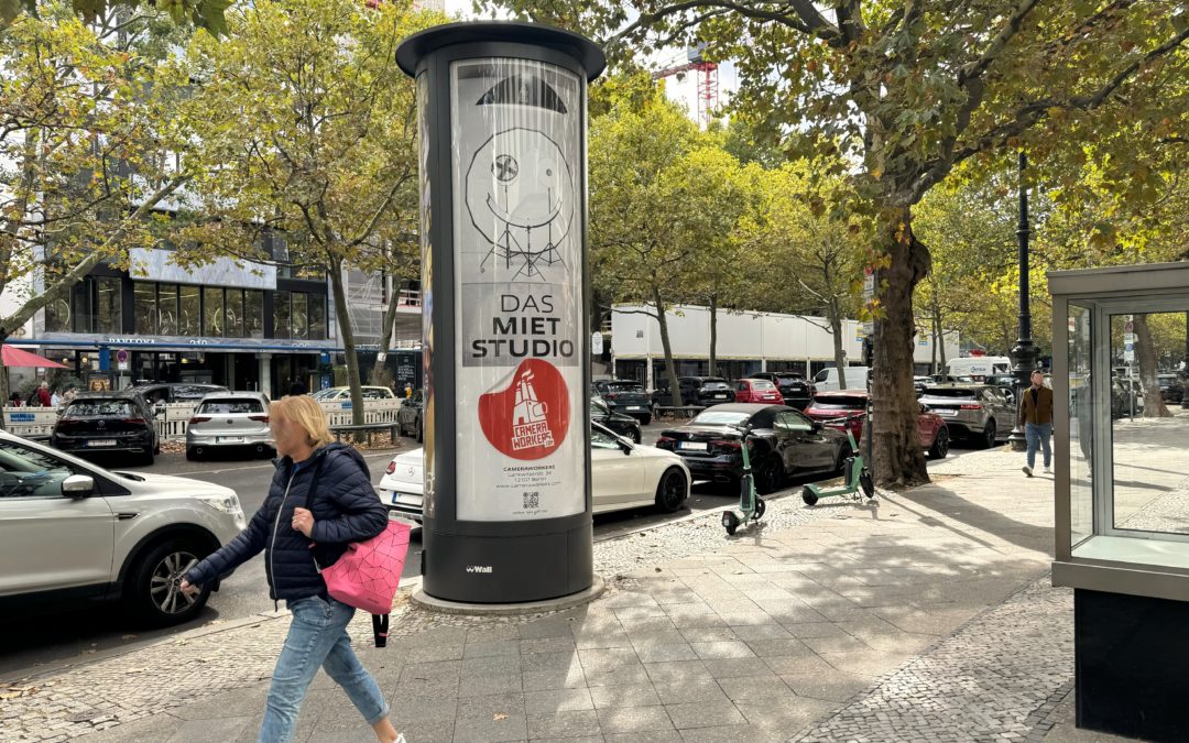 An den Straßen des Kurfürstendamm steht eine City Light Säule mit Plakatwerbung von Union Klischee und den Camera Workers. Das Motiv der Außenwerbung hat den Satz: „Das Mietstudio“ draufgedruckt, darunter ist ein Bild eines Fotostudios. Unter dem Bild ist des Logo abgebildet. Vor der Säule laufen Leute auf dem Fußgängerweg. Dahinter auf der Straße fahren und stehen Autos, man sieht viele Bäume und Geschäfte.